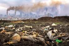 Plastic waste in the foreground, cityscape with distant smokestacks rising above the urban skyline in the background, creating a striking contrast