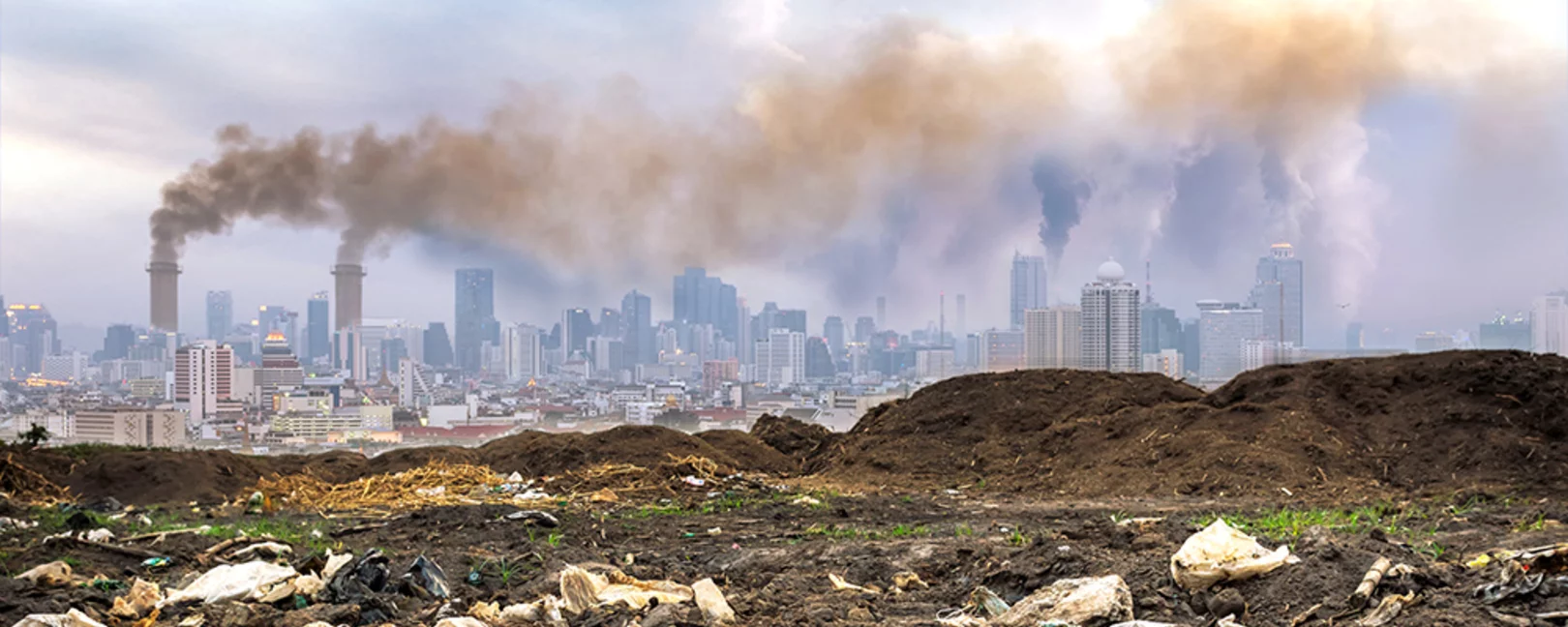 Plastic waste in the foreground, cityscape with distant smokestacks rising above the urban skyline in the background, creating a striking contrast